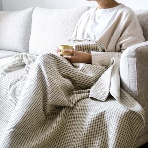 Mujer en sentada en sofa con la manta verdonce de algodón reciclado color olivo